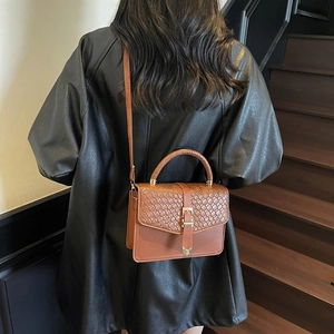 Sac à main marron à texture tressée avec poignée et fermoir doré porté par le mannequin