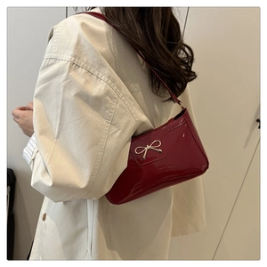 Detail of red patent leather shoulder bag with metallic bow on model's outfit