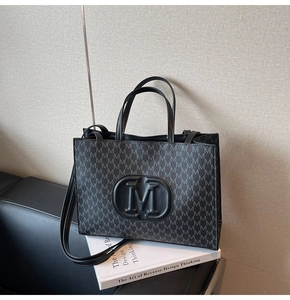 Detailed close-up of embossed round M logo and monogram print on black leather tote bag