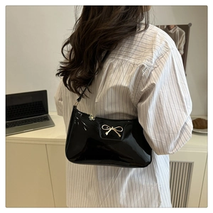 Detail of black patent leather shoulder bag with gold metal bow and petal zipper pull