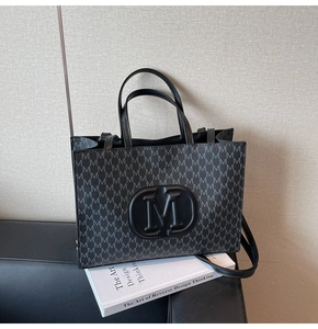 Detail of black tote bag featuring embossed M logo and monogram print with shoulder strap