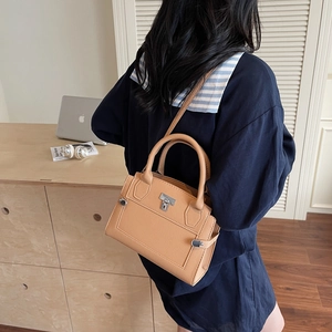 Elegant brown pebbled leather handbag with gold metal lock being carried by model