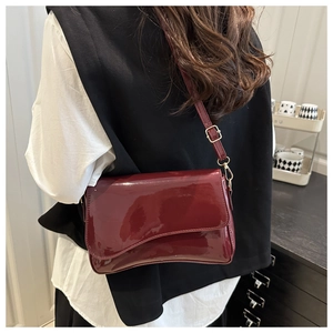 Detail of burgundy glossy patent leather shoulder bag with gold buckle on a thin strap