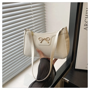 Detail of a creamy white baguette bag featuring a sleek finish and golden bow hardware