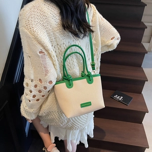 French woven mini bucket bag in cream fabric and green leather held by a model