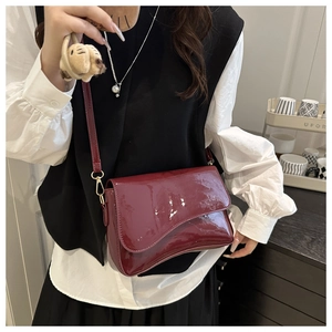 Detail of wine red glossy patent leather handbag with gold metal hooks and plush charm