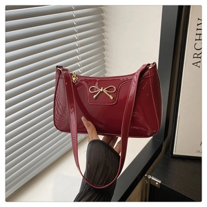 Detail of burgundy patent leather baguette bag featuring a gold metal bow and glossy finish