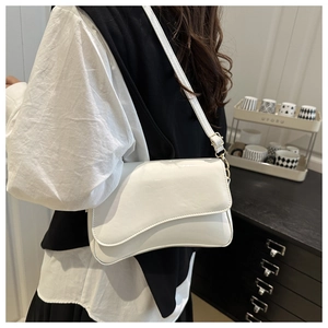 Detail of white glossy saddle bag featuring an asymmetrical flap and golden hardware