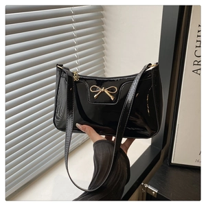 Detail of black patent leather baguette bag with golden bow and metal flower charm