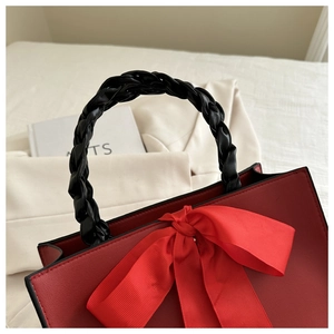 Détail d'un sac à main en cuir rouge foncé avec un grand nœud élégant et anse tressée