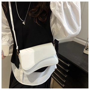 Detail of white glossy shoulder bag showing wavy flap edge and gold hardware