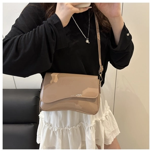 Detail of glossy beige square crossbody bag featuring a unique wavy irregular flap design