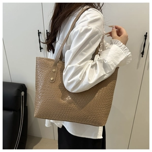 Detail of a brown woven tote bag featuring metallic rivet accents and a sleek shoulder strap