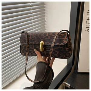 Detail of leopard print baguette bag with golden buckle held by a model in warm setting