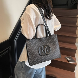 Grey tote bag with 'M' pattern texture and shoulder strap shown in a modern interior