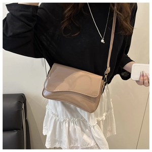 Detail of a beige patent leather crossbody bag with a wave flap worn by a model
