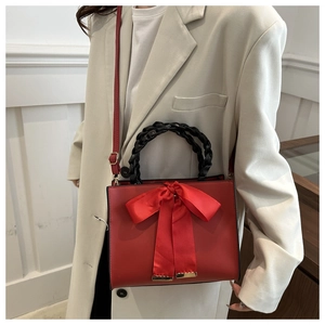 Détail d'un sac à main en cuir rouge avec nœud en satin et poignée tressée noire