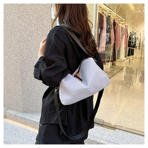 Outdoor shot of light gray nylon crossbody bag with bright orange zipper pull detail