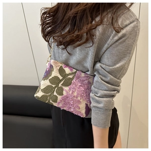 Détails de broderie florale et de paillettes mauves sur un sac tissé ivoire