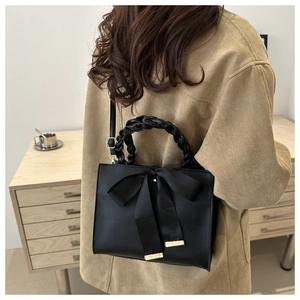 Détail de sac à main noir en cuir avec nœud en soie et poignée tressée sur le modèle