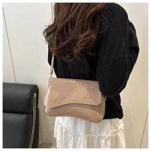 Detailed view of beige patent leather shoulder bag with gold hardware and curved flap