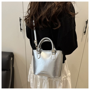 Detail view of silver tote bag with polished finish and adjustable strap worn by model