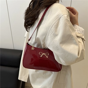 Glossy red faux leather baguette bag with golden bow hardware shown on model shoulder