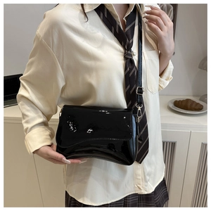 Detail of a black patent leather crossbody bag with gold hardware worn by a model