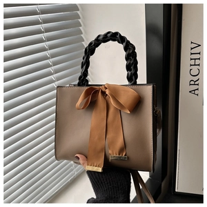 Detail of khaki handbag featuring black woven handles and a large decorative bow tie