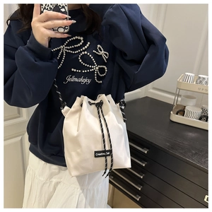 Détail du sac seau en nylon blanc avec étiquette Creative Cat et bandoulière rayée