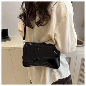 Detail shot of a black patent leather shoulder bag worn by a model in a casual indoor setting