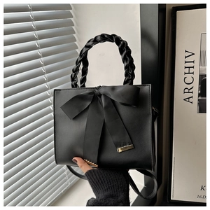 Detail of black leather handbag with woven handle and elegant satin bow decoration