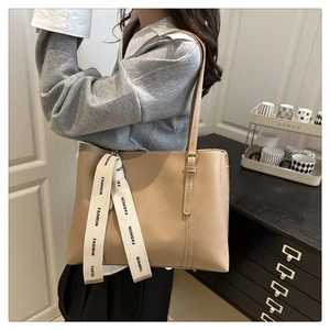 Detail of light khaki tote bag with fashion ribbon accessory on model in home setting