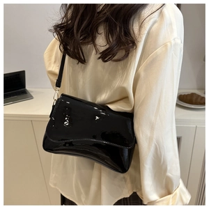 Detail of glossy black patent leather shoulder bag with gold buckles and wavy flap edge