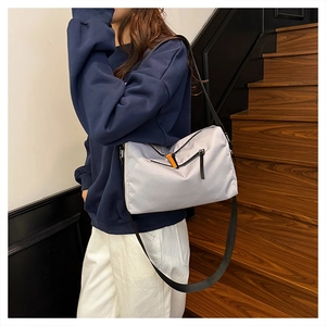 Detail of grey nylon crossbody bag featuring orange zipper pulls on a model on stairs