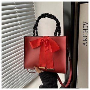 Detail of red leather handbag featuring a large bow and black woven top handle design