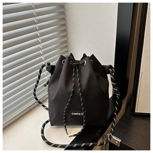 Détail du sac seau noir avec cordon, étiquette Creative C et bandoulière tissée bicolore