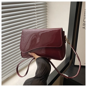Handheld shot of a wine red patent leather crossbody bag with a glossy finish and flap