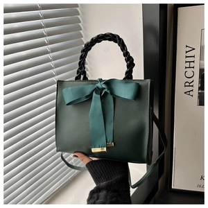 Detail of dark green handbag with silk ribbon bow and black woven handle close-up