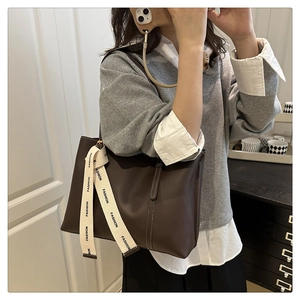 Detail of dark brown leather tote bag with stylish white fashion scarf on the strap