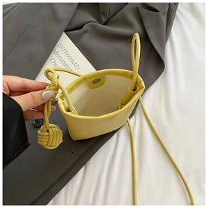 Close-up of yellow leather phone bag with magnetic snap and woven ball accessory