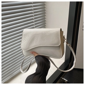 Detail of creamy white patent leather crossbody bag with unique curved wave flap design