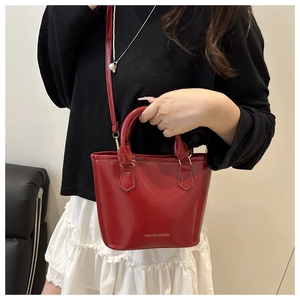 Red glossy leather bucket bag with gold lettering details shown in a lifestyle shot
