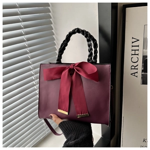 Detail of burgundy bridal handbag featuring a large bow with gold metallic edge details