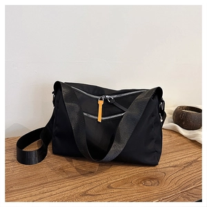 Detailed view of black nylon messenger bag with orange zipper pull on wooden surface