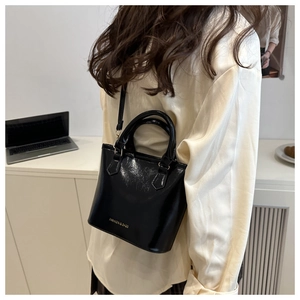 Glossy black patent leather bucket bag with gold lettering shown in a modern office setting