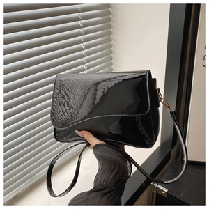 Detail of black glossy shoulder bag featuring a unique wavy curve flap and patent leather texture