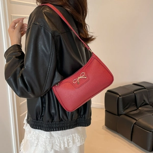 Red pebbled leather shoulder bag with a gold metal bow and thin strap shown on a model