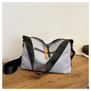 Macro view of nylon messenger bag featuring orange leather zipper pull and wide strap