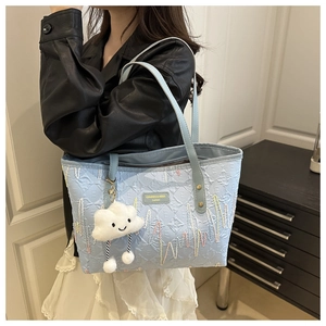 Dettaglio della borsa tote azzurra con ricamo a onde e ciondolo a nuvola di peluche
